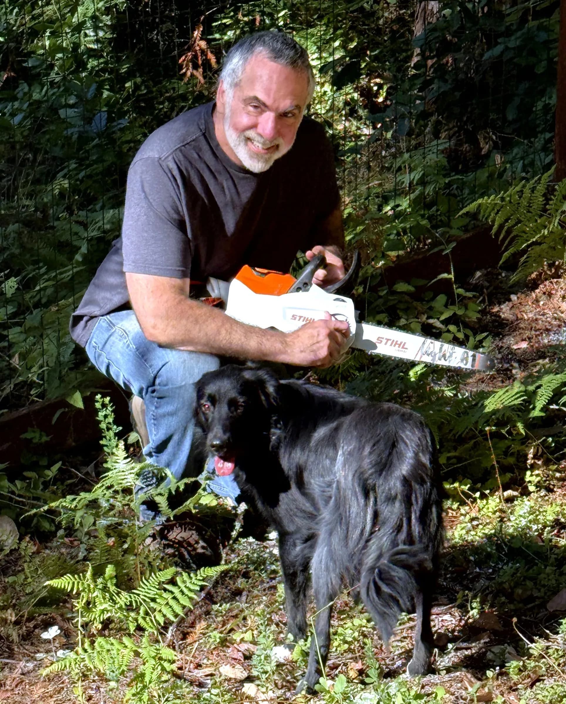 Craig Winter outdoors with his dog, holding a chainsaw in a wooded Felton-area setting